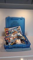 Blue plastic LEGO carry case open showing various LEGO instruction manuals inside.