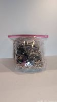 Front view of a plastic zip-lock bag filled with assorted jewelry pieces of varying materials and styles.