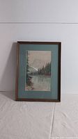 Full view of the framed watercolor landscape painting showing the trees, water, and mountain background.