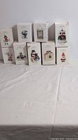 Nine Hallmark Christmas ornaments in original boxes, assorted holiday themes, positioned on a white surface.