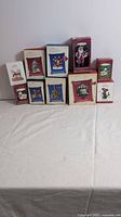 Overall view of 11 Hallmark Keepsake Christmas Ornaments in original boxes grouped together on white surface.