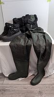 Green thigh-high hip waders with attached boots, displayed on a white cloth backdrop.