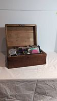 Medium brown wooden box with hinged lid open, showing assorted beading supplies including beads and tools inside.