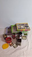 Five decorative tins in front with the two craft bead boxes stacked behind containing various beads and pins.