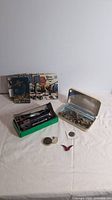 Wide view of the lot showcasing the vintage model train in green box, needle books in background, metal container with assorted jewelry, and coins spread on the table.
