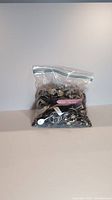 Plastic zip bag containing various watches and jewelry including visible watch straps in pink and white, assorted designs and metals packed together.