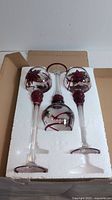 Three glass candle holders with poinsettia flower designs packed in white foam padding inside original box.
