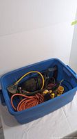 Blue storage bin filled with power tools and cords, viewed from above and side angle, showing overall contents of the lot.