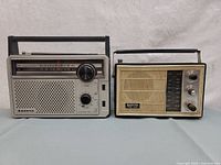 Two vintage Sanyo portable radios side by side; silver radio on left with carrying handle, yellow radio on right with cream grille and knobs