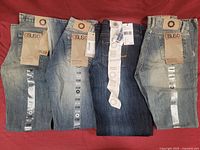 Four pairs of new jeans laid out on red background, tags attached, showing various light and dark denim shades.