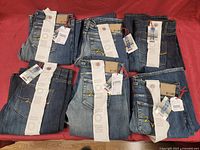 Overview of six folded pairs of jeans on red background, showing variety of denim washes and tags