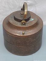 Side angle view showing engraved patterns and the handle of the brass tiffin carrier with patina and verdigris.