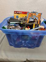 Photo of blue plastic bin filled with assorted LEGO bricks, some partially assembled sets and instruction manuals including LEGO Ninjago and castle-themed sets.