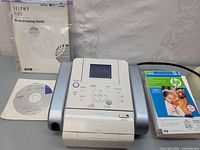 Canon SELPHY DS810 printer with user manual, software CD, and pack of HP photo paper on display surface.