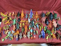Photo showing a wide arrangement of diverse dinosaur and reptile toy figures placed on a red cloth background.