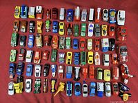 Top-down image showing 70 assorted die-cast cars and trucks arranged in rows on a red surface.