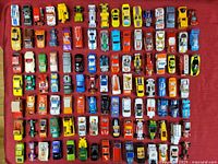 Overhead view of around 60 assorted die cast cars arranged on a red background, showing diversity in colors and car models.