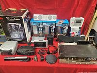 Full view of lot with karaoke system box, car boost boxes, photo printer pack, portable CD player, headphones, and other small electronics visible