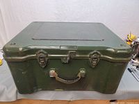 Front view of the green plastic military storage box showing the metal latch locks and handle.