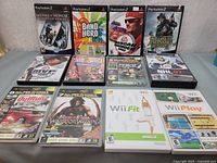 Photo showing front covers of 9 empty PlayStation 2 game cases and 2 Wii game cases arranged on a flat surface.
