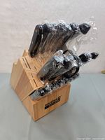 View of the Ronco Six Star+ cutlery set in the honey oak wooden block with black handled knives wrapped in plastic.