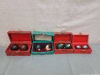 Front view of all four pairs of worry balls displayed in their individual decorative boxes, showing different styles and colors.