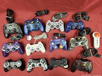 Photo showing all 14 video game controllers laid out together on red fabric.