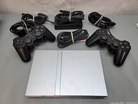 PlayStation 2 slim model SCPH-77001 console with two DualShock 2 controllers and cables arranged for sale.