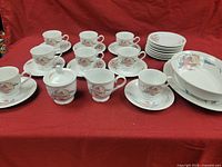 Full set of tea cups, saucers, sugar bowl with lid, creamer, and additional plates displayed on red background