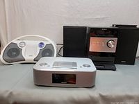 Photo showing Philips Docking Entertainment System in white and silver front and a Sony Micro Hi-Fi Shelf System with black exterior and metallic front panel with two accompanying speakers.