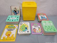 Full display of 20 Sesame Street educational card game sets, "Guide for Parents" booklet, and yellow carrying case.