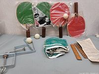 Overall view of the vintage table tennis set including paddles, balls, net, clamps, rulers and paper sheet.