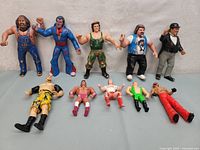 Wide view of all 10 vintage WWF wrestling figures arranged on grey background showing various poses and colors including a wrestling manager/referee figure.