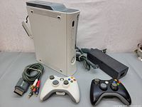Xbox 360 Pro white console standing upright with white and black wireless controllers in front, AV composite cables and power supply visible.