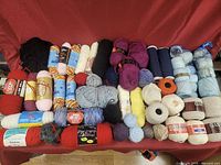 Full lot of yarn, wool, and thread rolls spread over a surface showing variety of colors and textures.