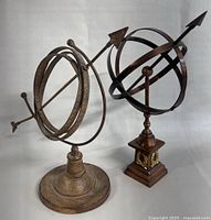 Both antique armillary globes side by side showing size, shape, and finish differences.