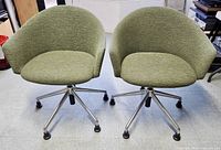Front view of both swivel chairs showing green fabric upholstery and rounded design.