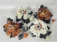 Two pairs of lotus flower-shaped candleholders, one white jade pair with red bead stamens and one brown glass pair with yellow and red bead stamens, shown together.