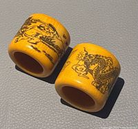 Pair of yellow hand carved Chinese thumb rings showing dragon and figure designs on sides.