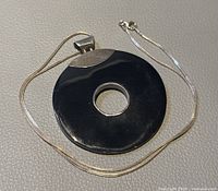 925 silver necklace with large black circular pendant with a central hole, shown on light textured background.