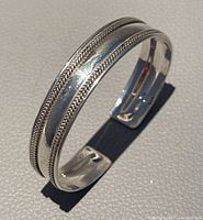 Sterling silver open cuff bracelet standing on edge showing braided detail and shine