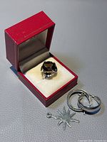 Overall view of ring in red box with earrings and pendant charm laid outside.