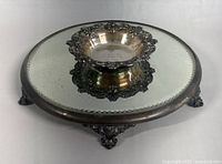 Top angle view showing the reflective surface, silver plated decorative footed base with ornate floral and scroll work, minor tarnish visible.