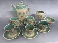 Full coffee set displayed, showing coffee pot, creamer, six cups and six saucers with matching floral pattern and pastel green interiors.