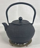 Front angle view of the black cast iron Asian teapot on round metal stand