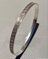 View of the silver bangle showing engraved Greek key decorative pattern on the outer surface.