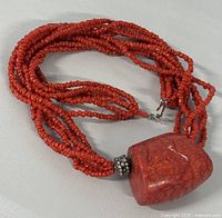 Close-up photo showing multiple strands of small natural coral beads with a large polished natural coral stone pendant and decorative metal bead.