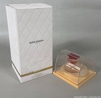 White quilted box labeled Boucheron next to transparent display case with peach base holding Fiorilu Eau de Parfum bottle.