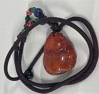 Close-up image of the hand carved reddish Nanhong agate pendant on a dark braided cord necklace with multicolored beads.