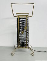 Front view of the brass floor heat lamp showing black mesh panels, decorative brass leaves, curled feet base, and electrical cord.
